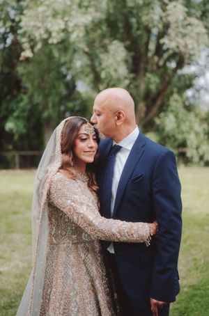 A romantic outdoor wedding moment featuring a bride in a sparkly gown and groom in navy suit beneath blooming trees.