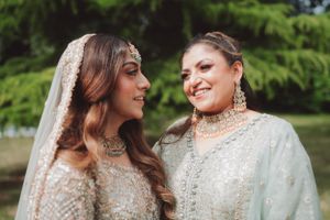 Two women in elegant sparkly traditional wedding attire smiling outdoors.