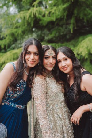 Three women in formal dresses pose together at an outdoor wedding celebration.