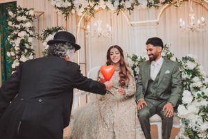 Wedding celebration moment with entertainer presenting heart decoration to seated couple.