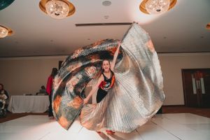 Dancer performing with flowing silver and orange fabric during wedding reception.