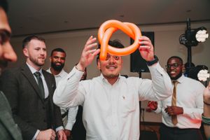 Wedding guest entertains crowd with orange inflatable prop at reception party.