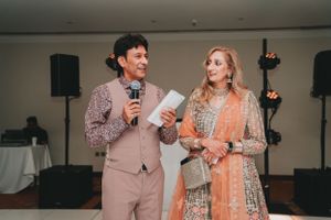 Event hosts in formal attire speaking into microphones during wedding celebration.