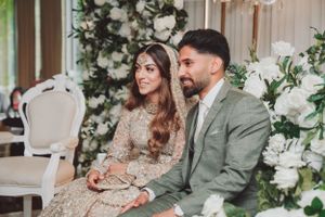 Couple in traditional South Asian wedding attire sitting together among floral decorations.