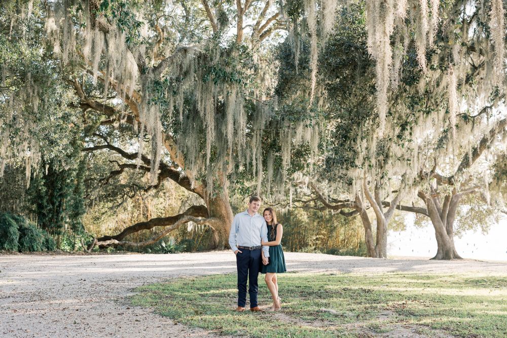 Engagement photo beneath moss-draped oak trees in Southern garden setting.