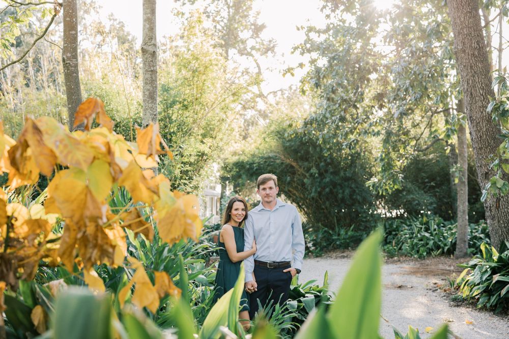 Couple poses together on garden path with yellow flowers in foreground.