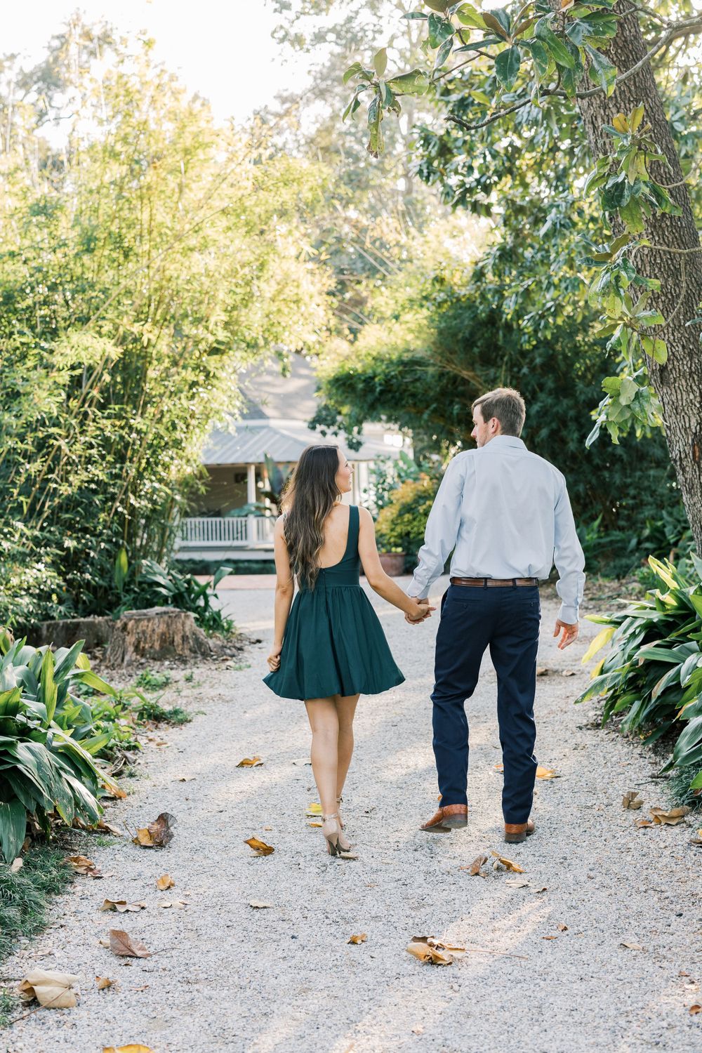 Couple walking hand in hand down scenic garden path with house in background.