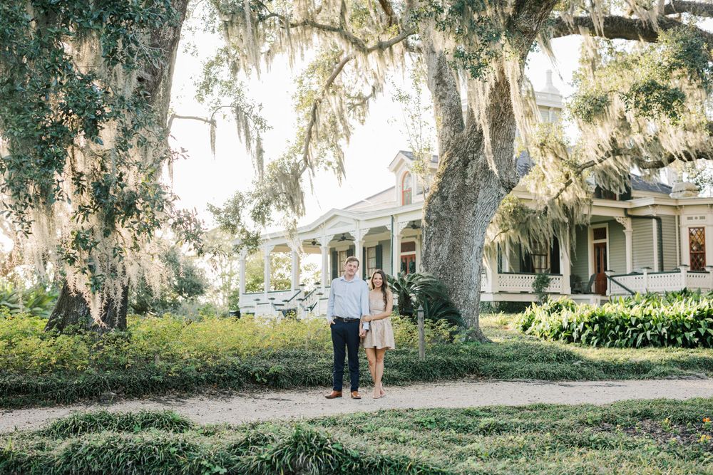 Couple stands under Spanish moss draped trees in front of Southern mansion.