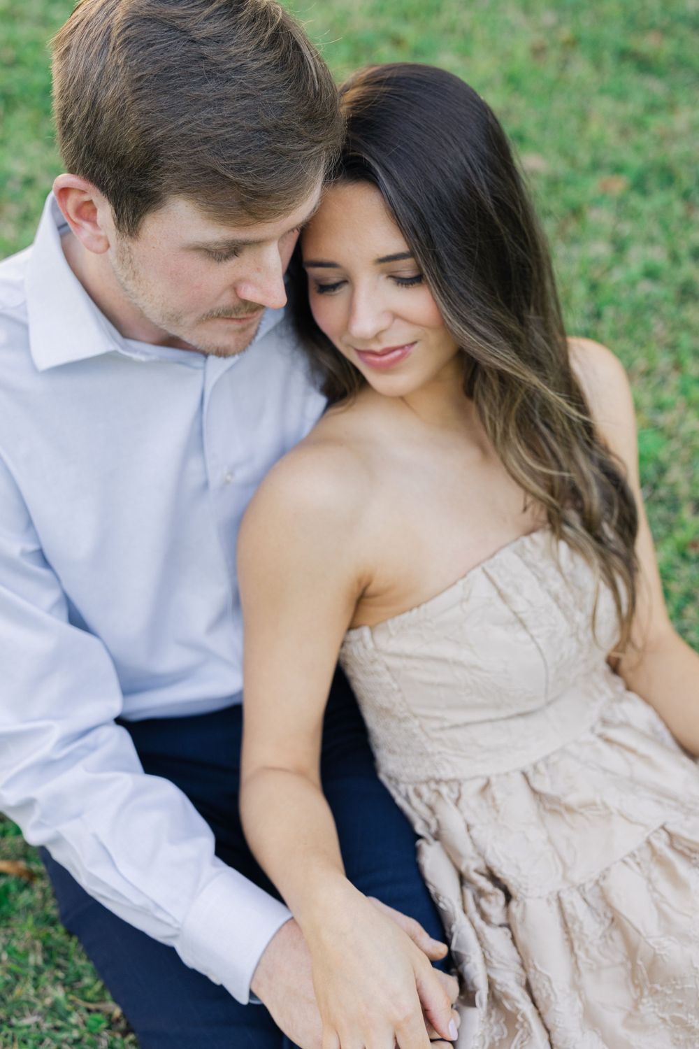 Intimate moment captured between couple sitting close together on grass.