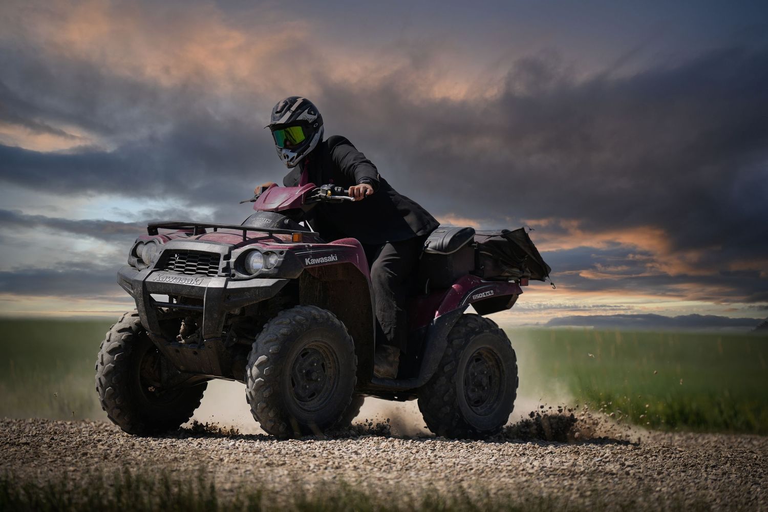 ATV rider in protective gear silhouetted against dramatic sunset sky on dirt path.