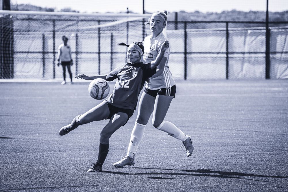 Two soccer players compete for ball possession during outdoor match.