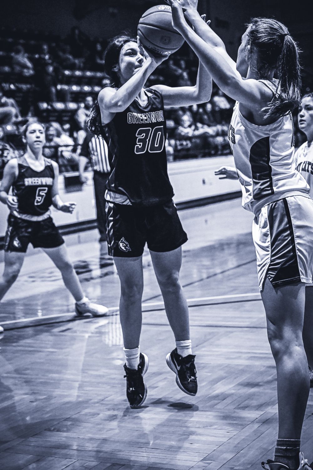 Basketball player takes a jump shot while being defended during an intense game moment.