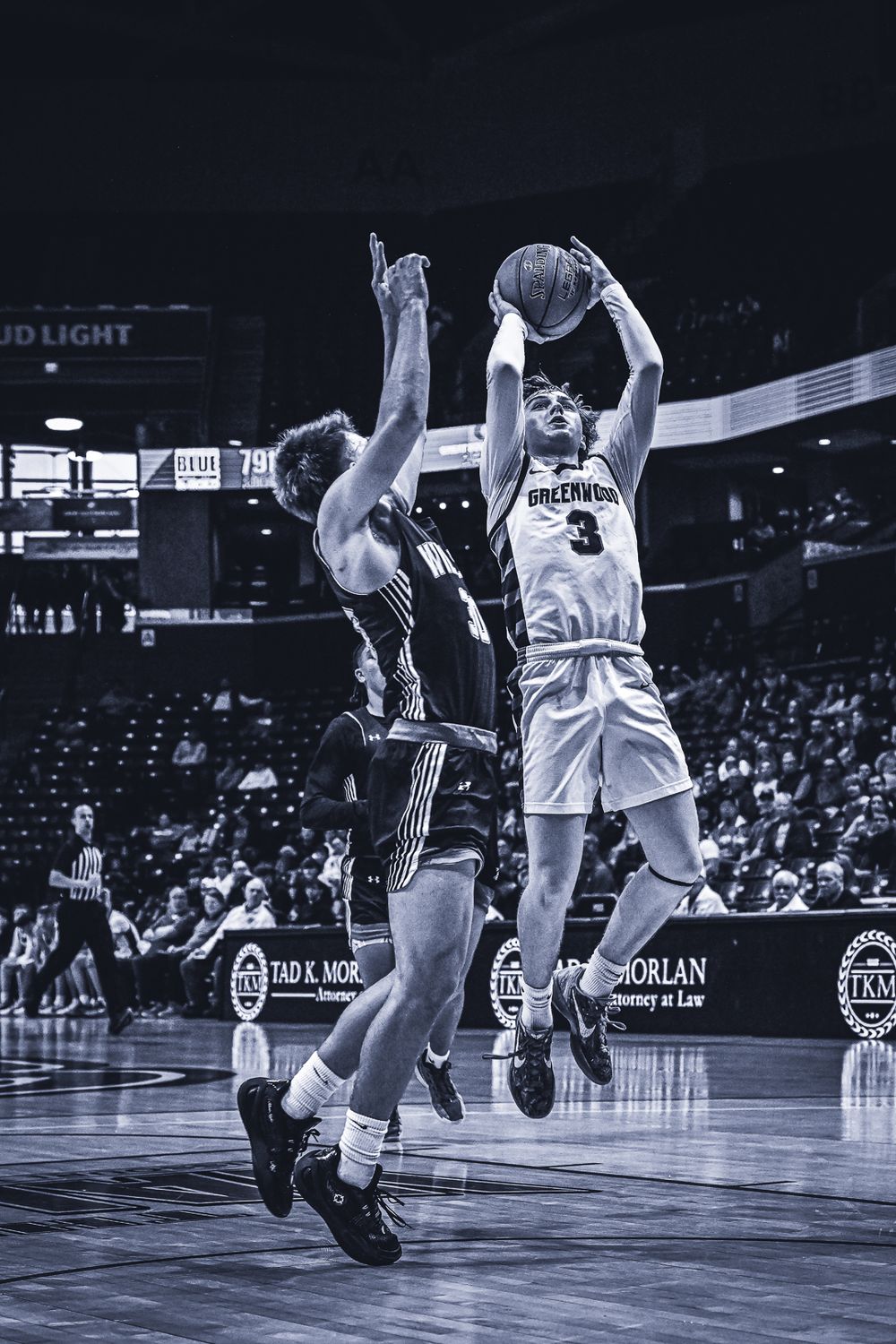 Basketball player takes jump shot while defender tries to block in intense game action.