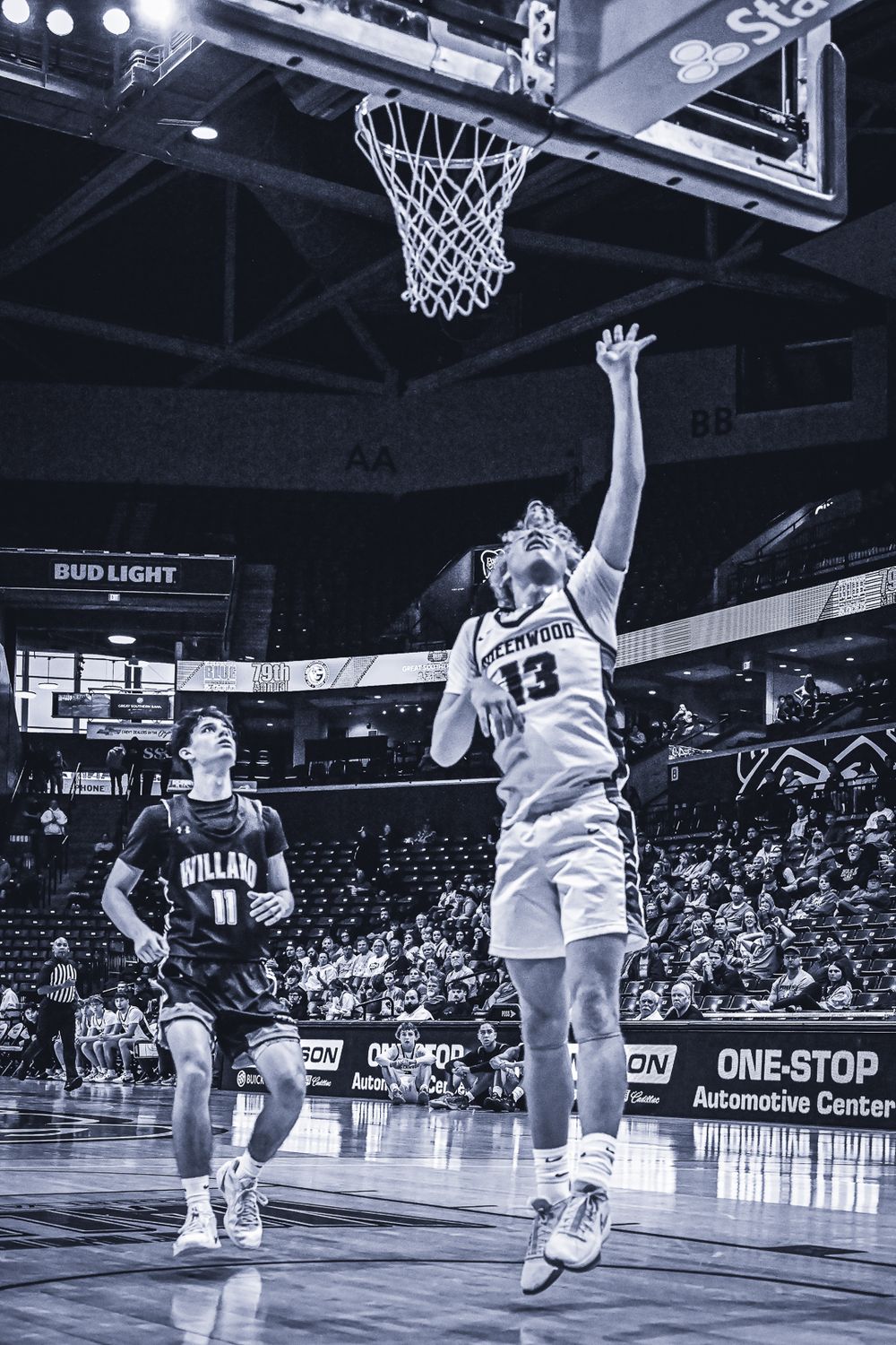 Basketball player reaches for layup near basket during competitive game.