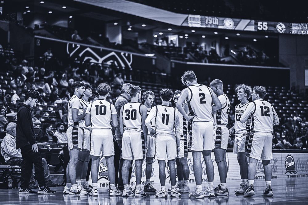 Basketball team lines up on court during game break in black and white photo.