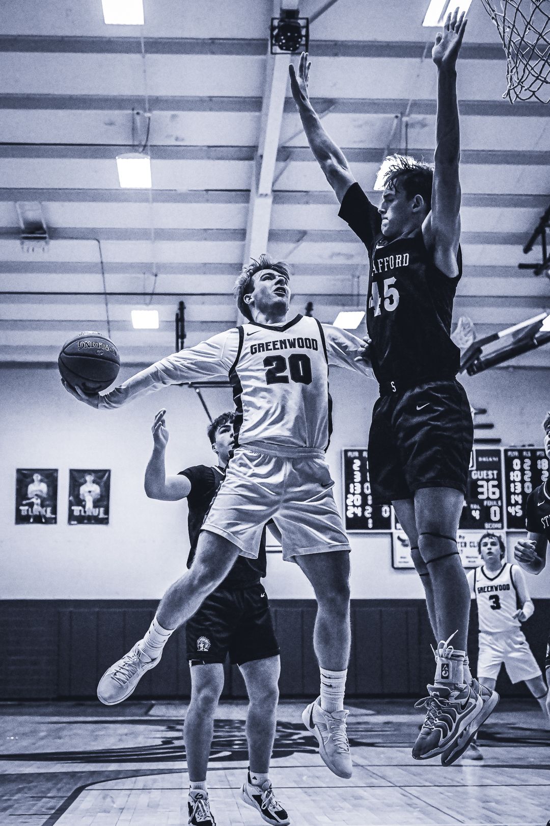 Black and white action shot of basketball players competing for a layup during an indoor game.