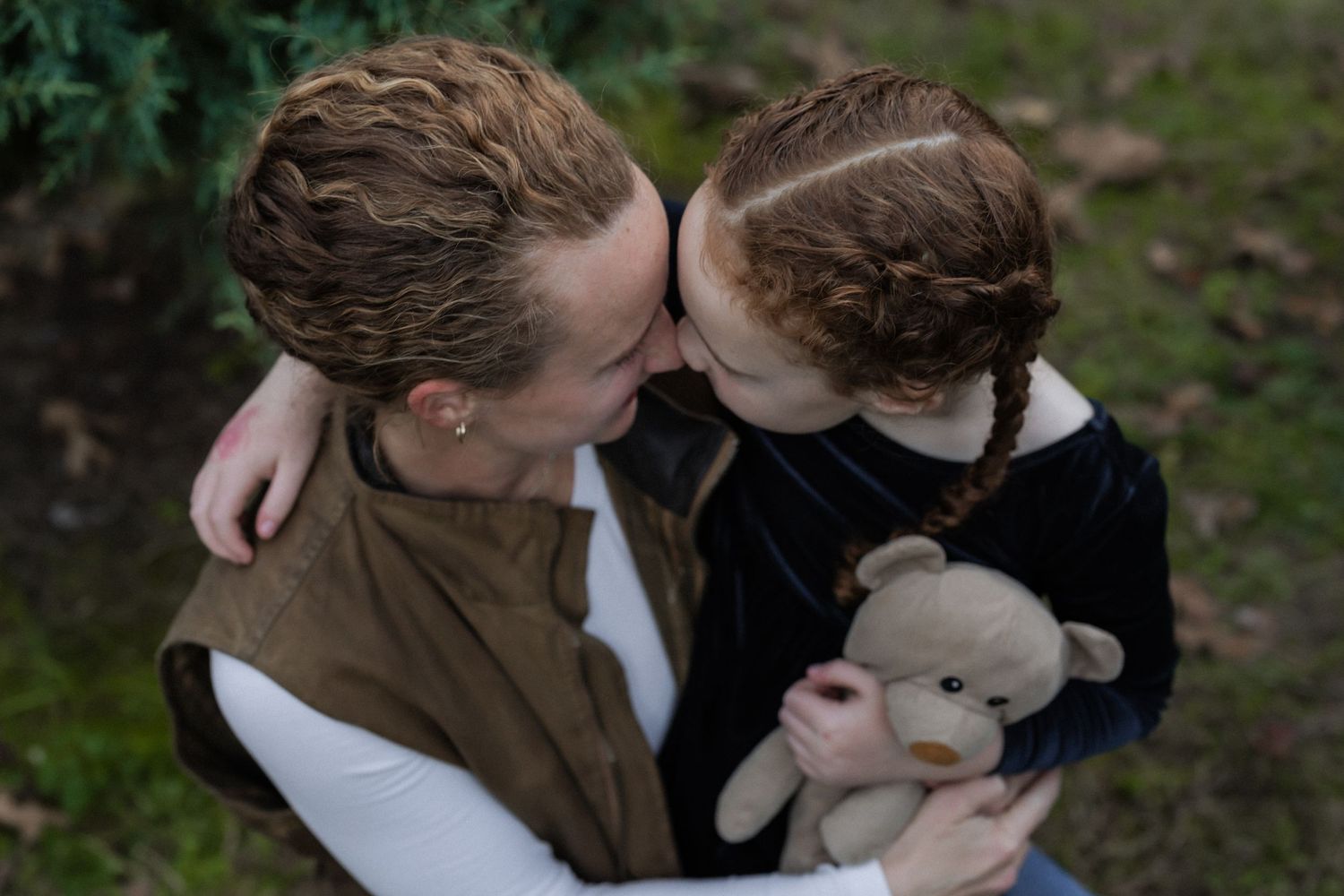 Two people embrace tenderly outdoors while holding a small plush toy rabbit in their arms.