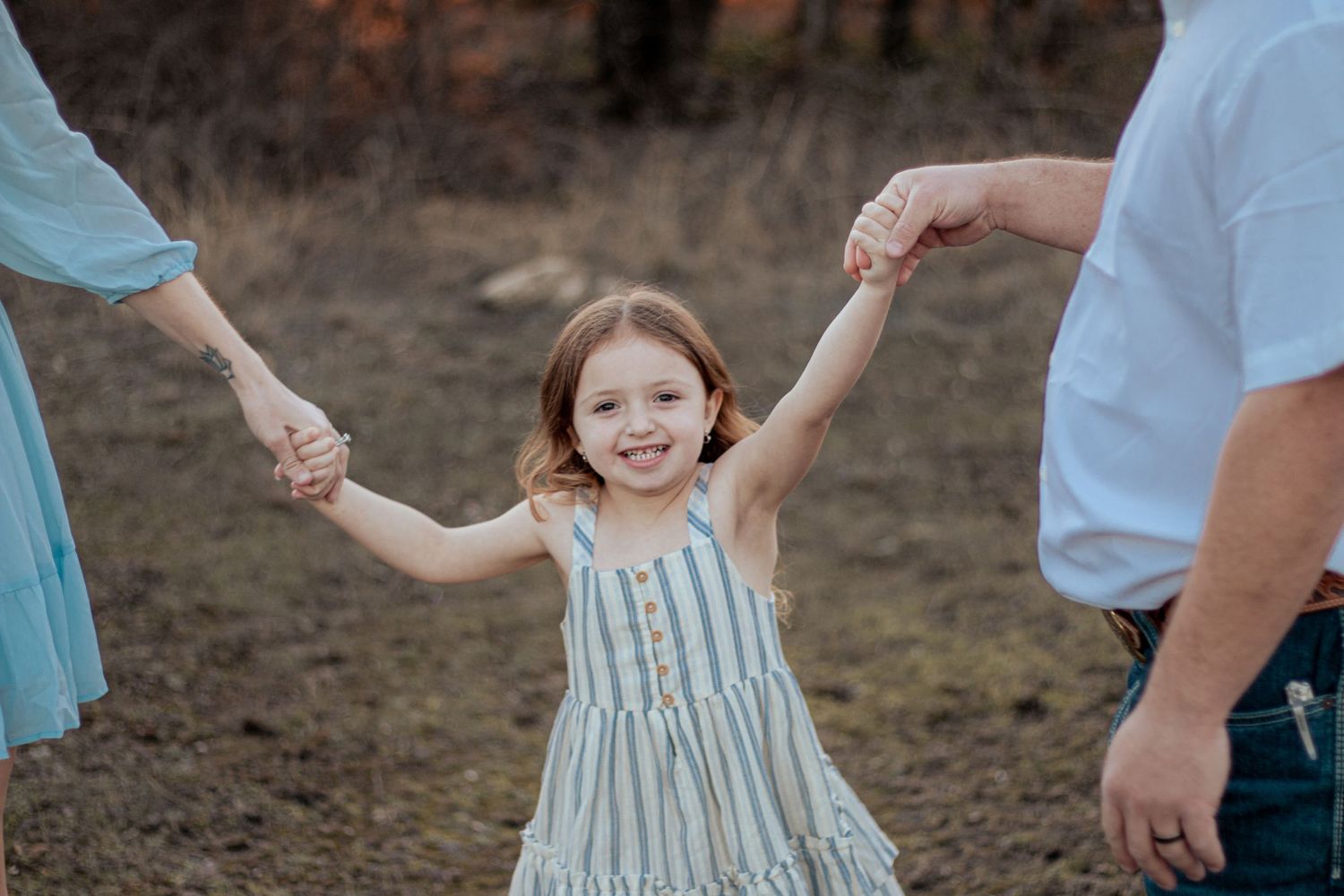 A child in a striped dress holds hands with adults while walking outdoors at dusk.