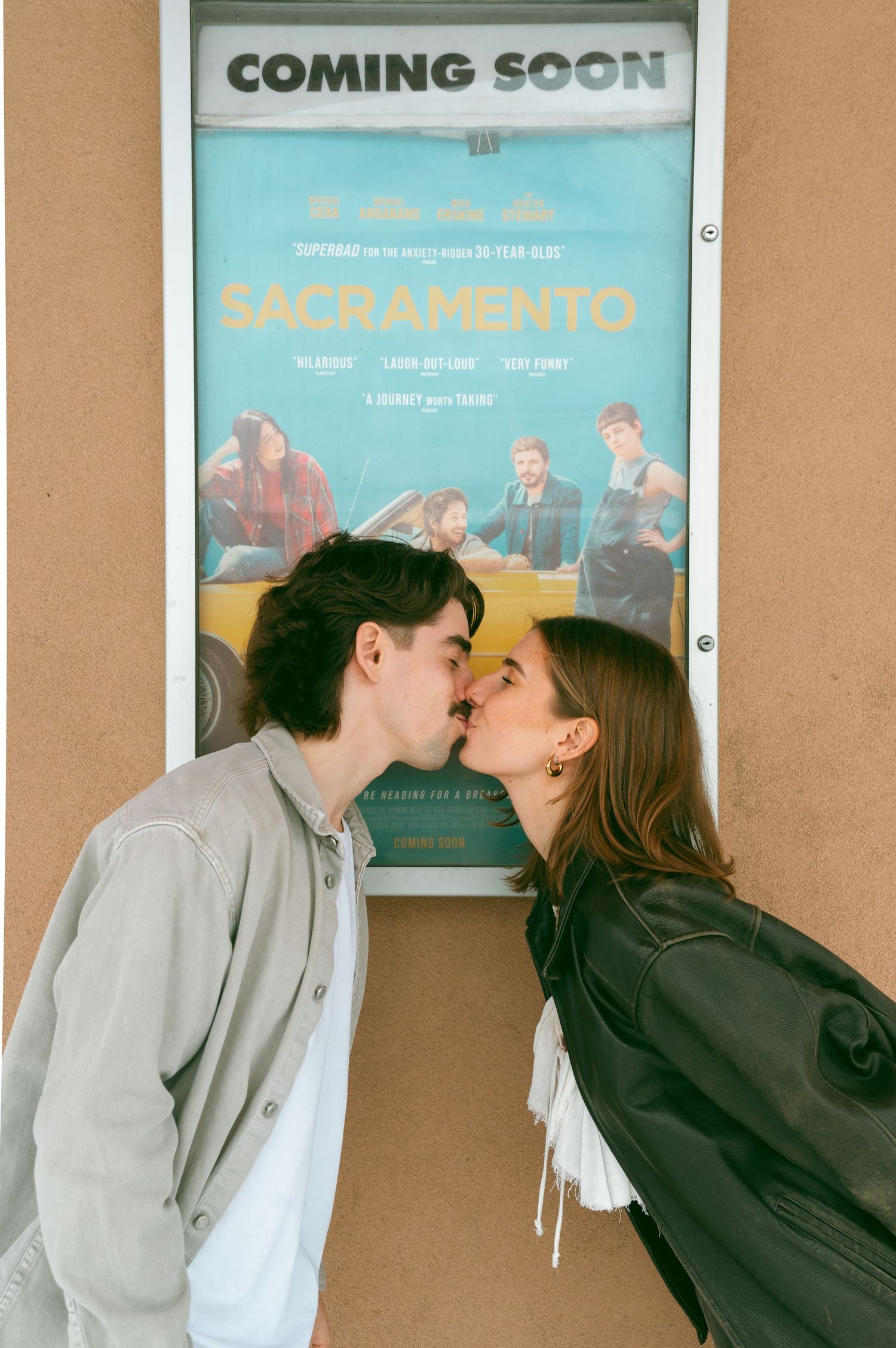 A romantic couple kisses in front of a blue movie poster that says 'Coming Soon' at a theater at the Roxy Theatre, Saskatoon Saskatchewan.