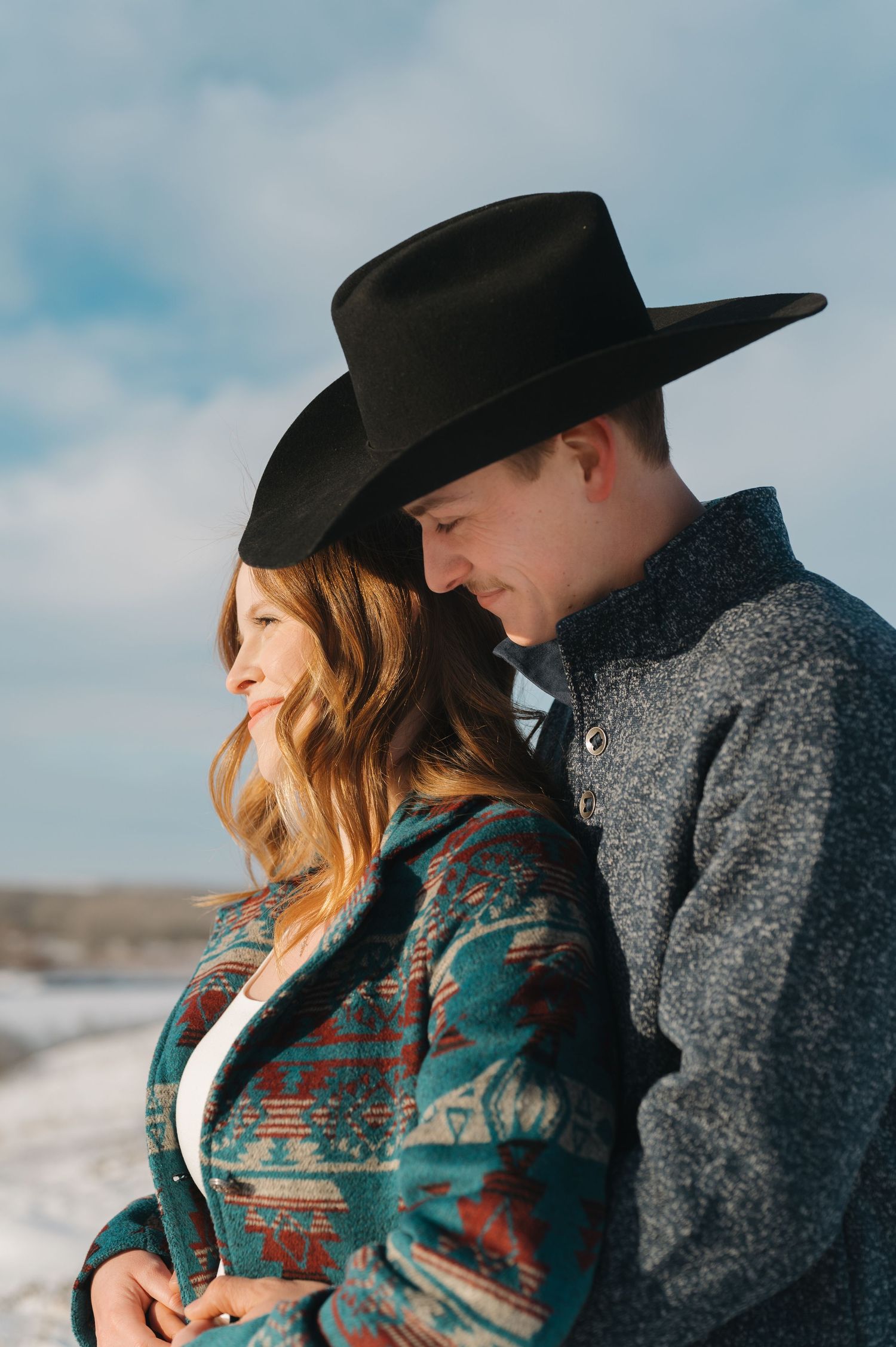 A couple in winter clothing shares a sweet moment against a snowy backdrop.