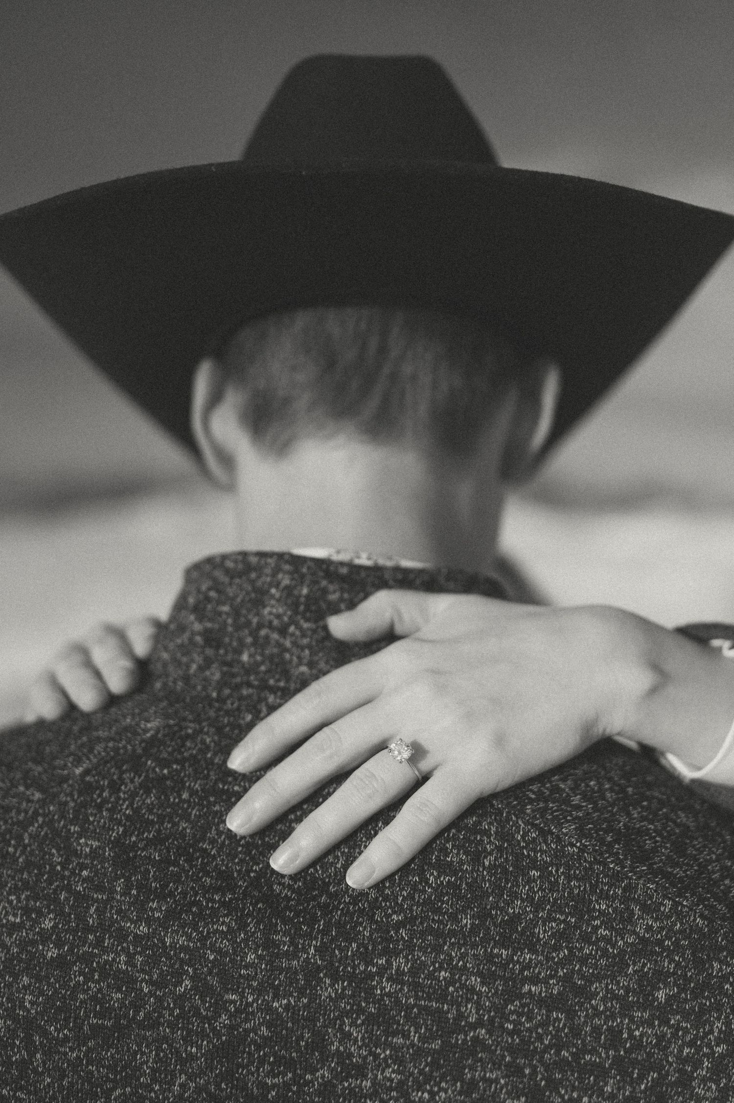 Close-up of hands embracing person wearing cowboy hat in black and white.