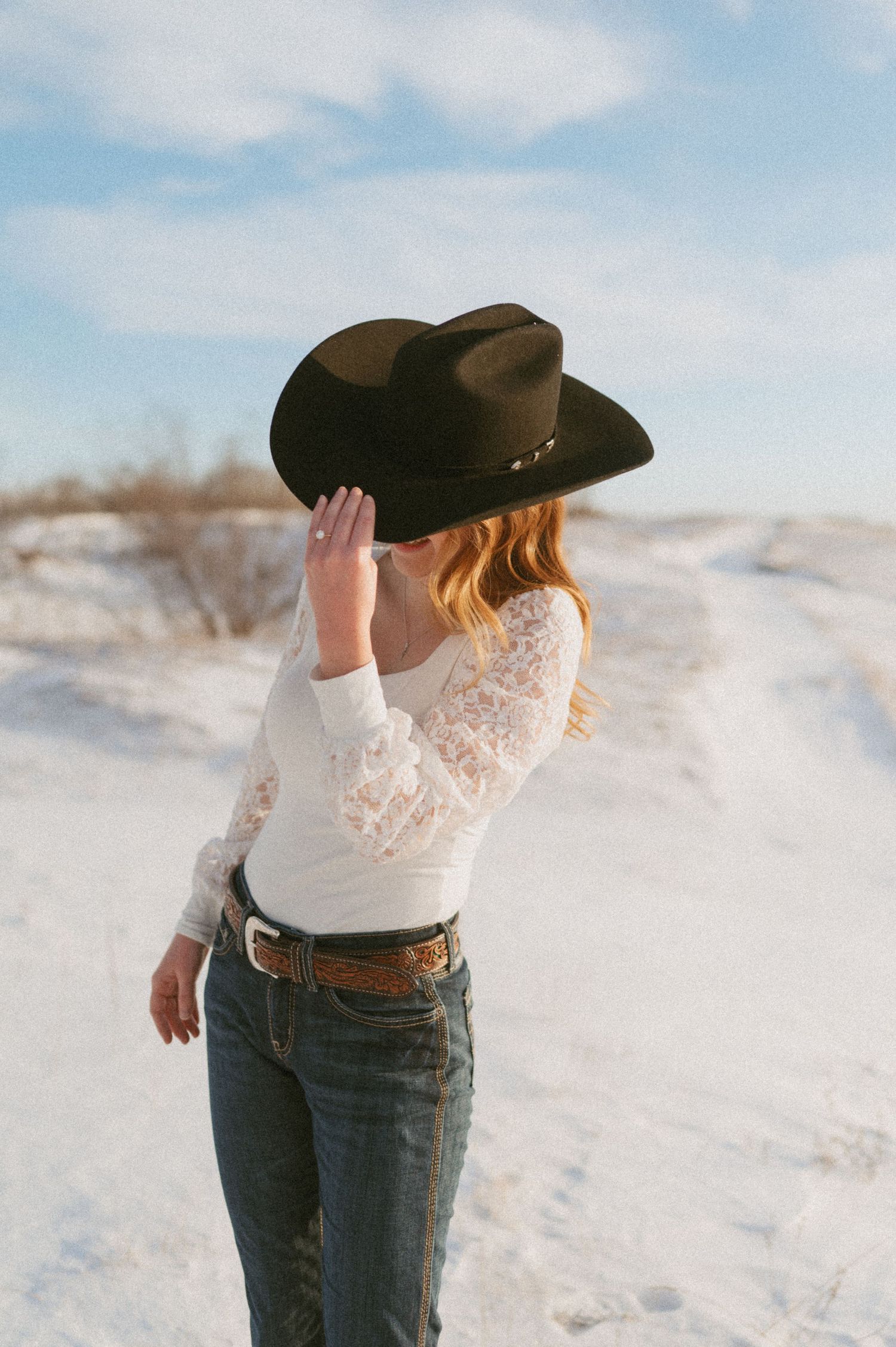A person in western attire with a cowboy hat stands in a snowy field.