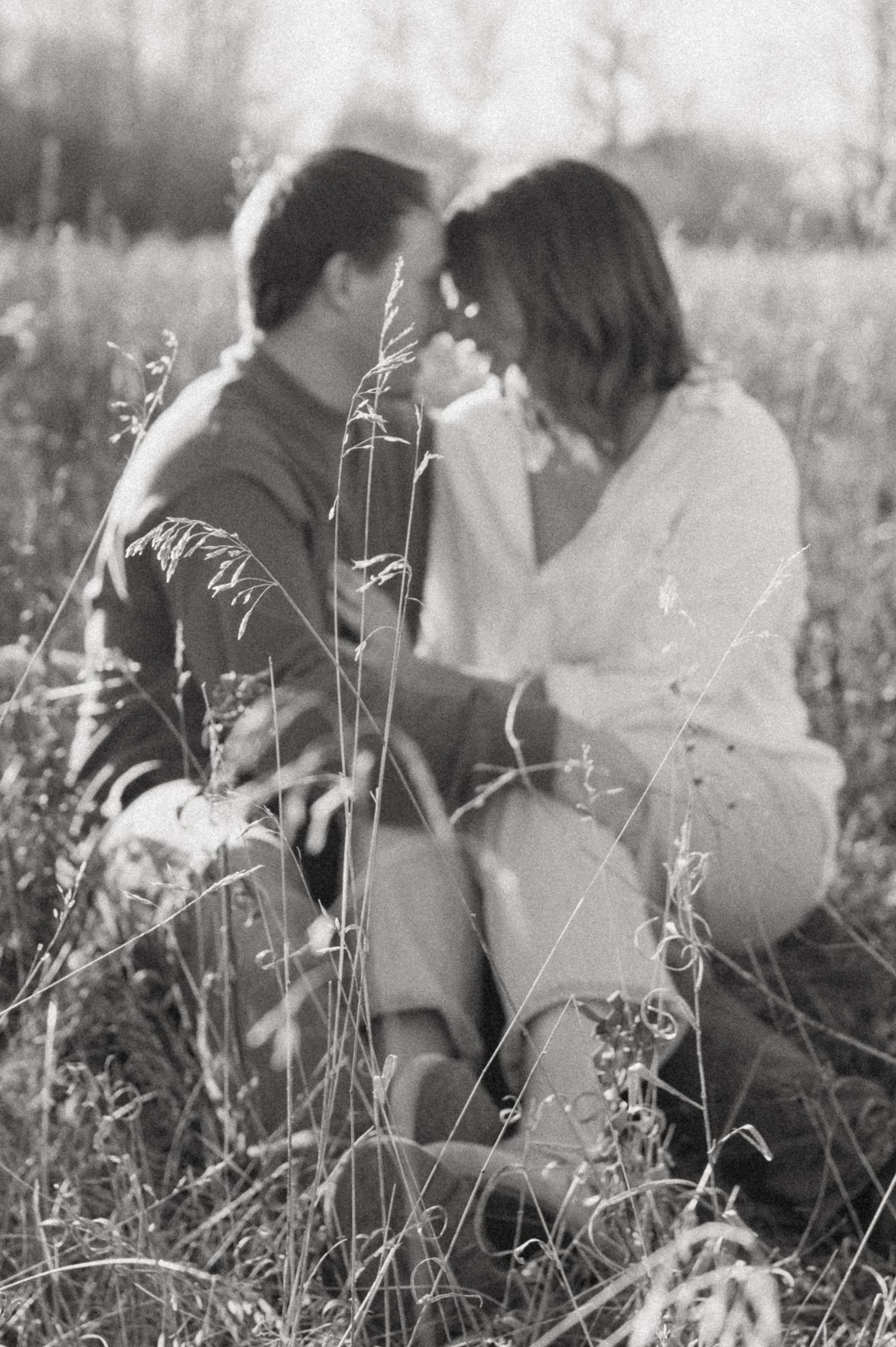 Black and white image of couple sitting intimately in a meadow.