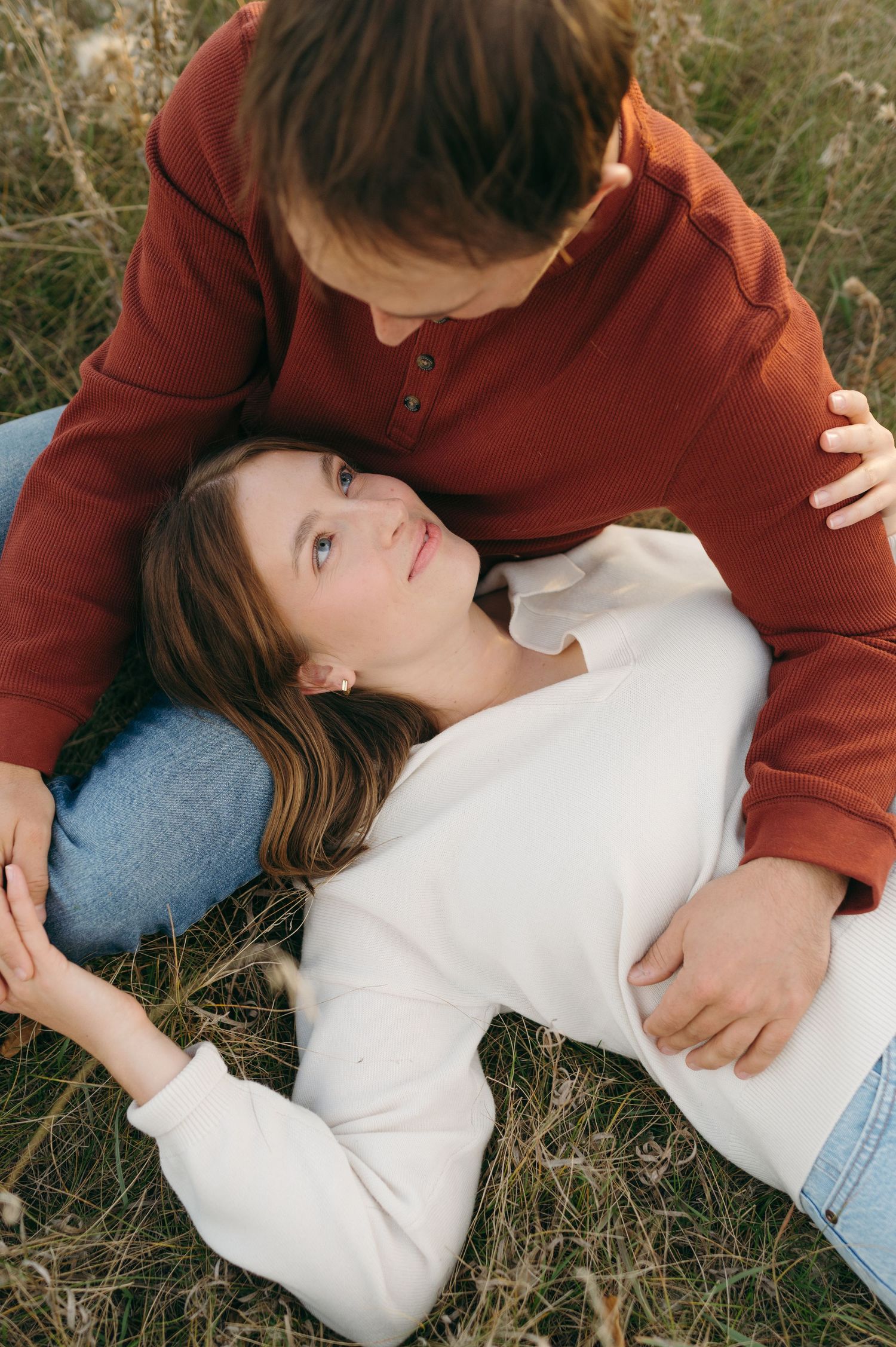 A couple shares an intimate moment lying in tall grass outdoors.