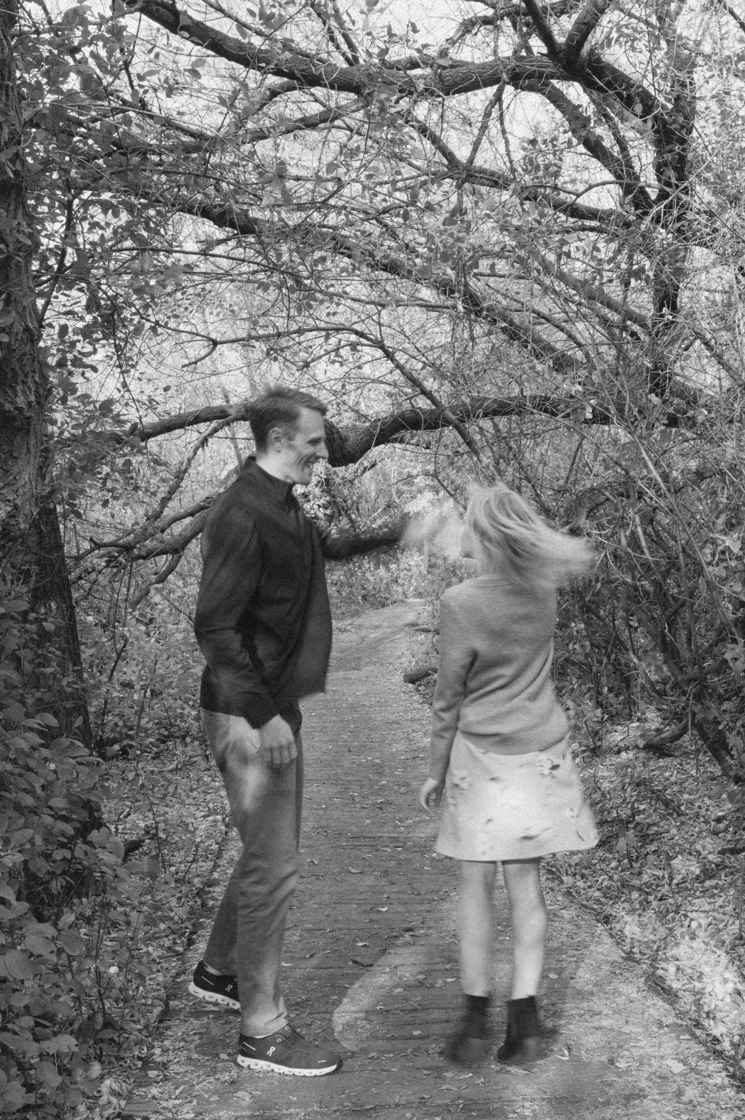 Black and white photo of playful couple on wooded path.