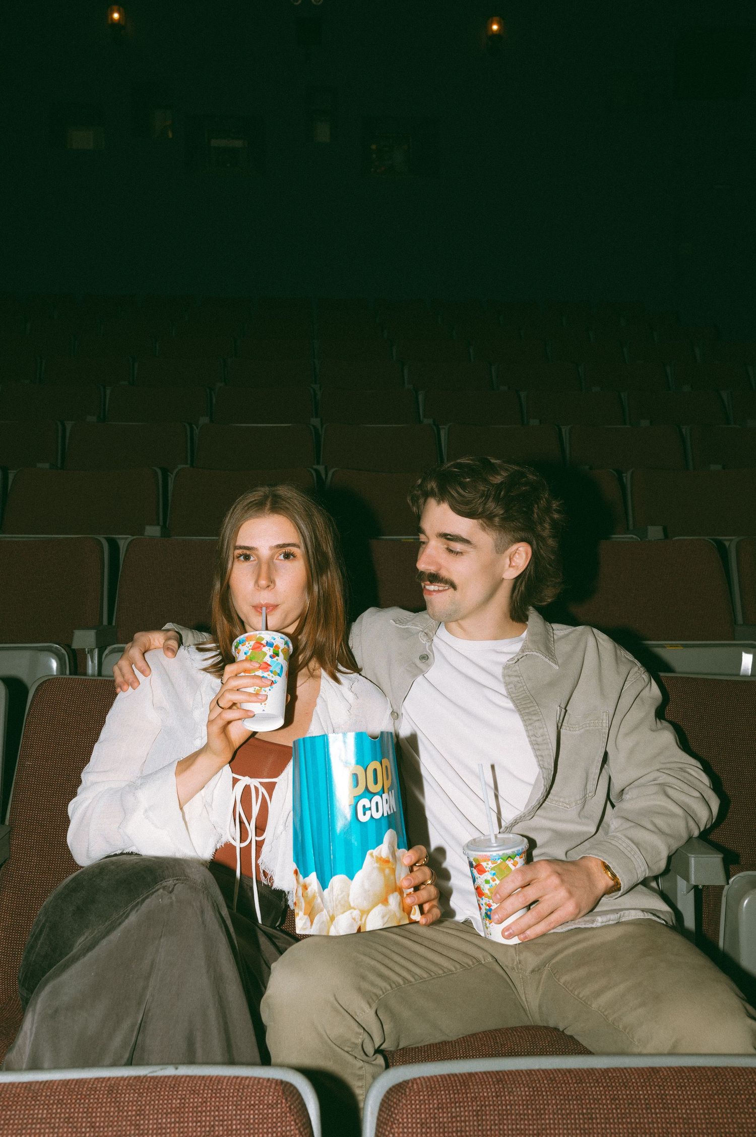 A series of film grain photos showing a couple drinking beverages and sharing popcorn in a dimly lit movie theater.