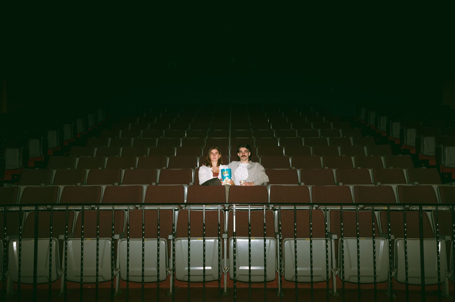 Two people sit alone in an empty theater auditorium illuminated by a soft glow in the darkness at the Roxy Theatre, Saskatoon Saskatchewan.