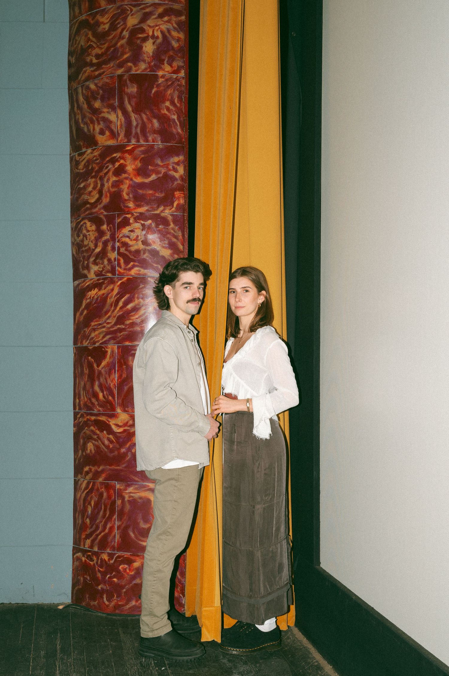Couple in casual attire stand together against a wall with red marbled pattern and yellow accent stripes at the Roxy Theatre, Saskatoon