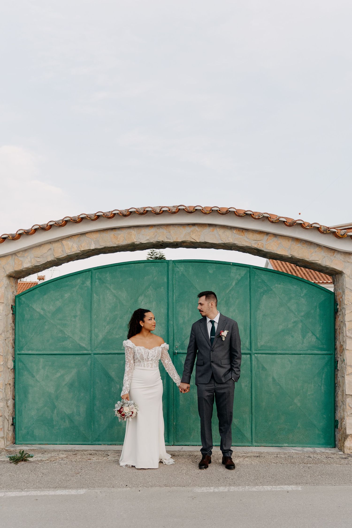Creative wedding portrait against green doors with stone archway architecture.