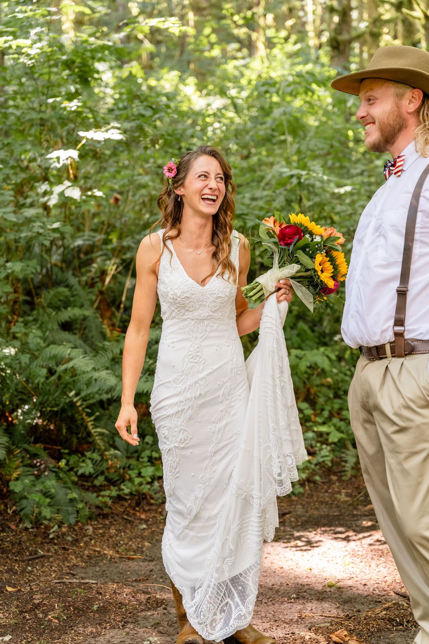 A couple sharing a joyful moment on their wedding day in the woods, with sunflowers and a lace dress.