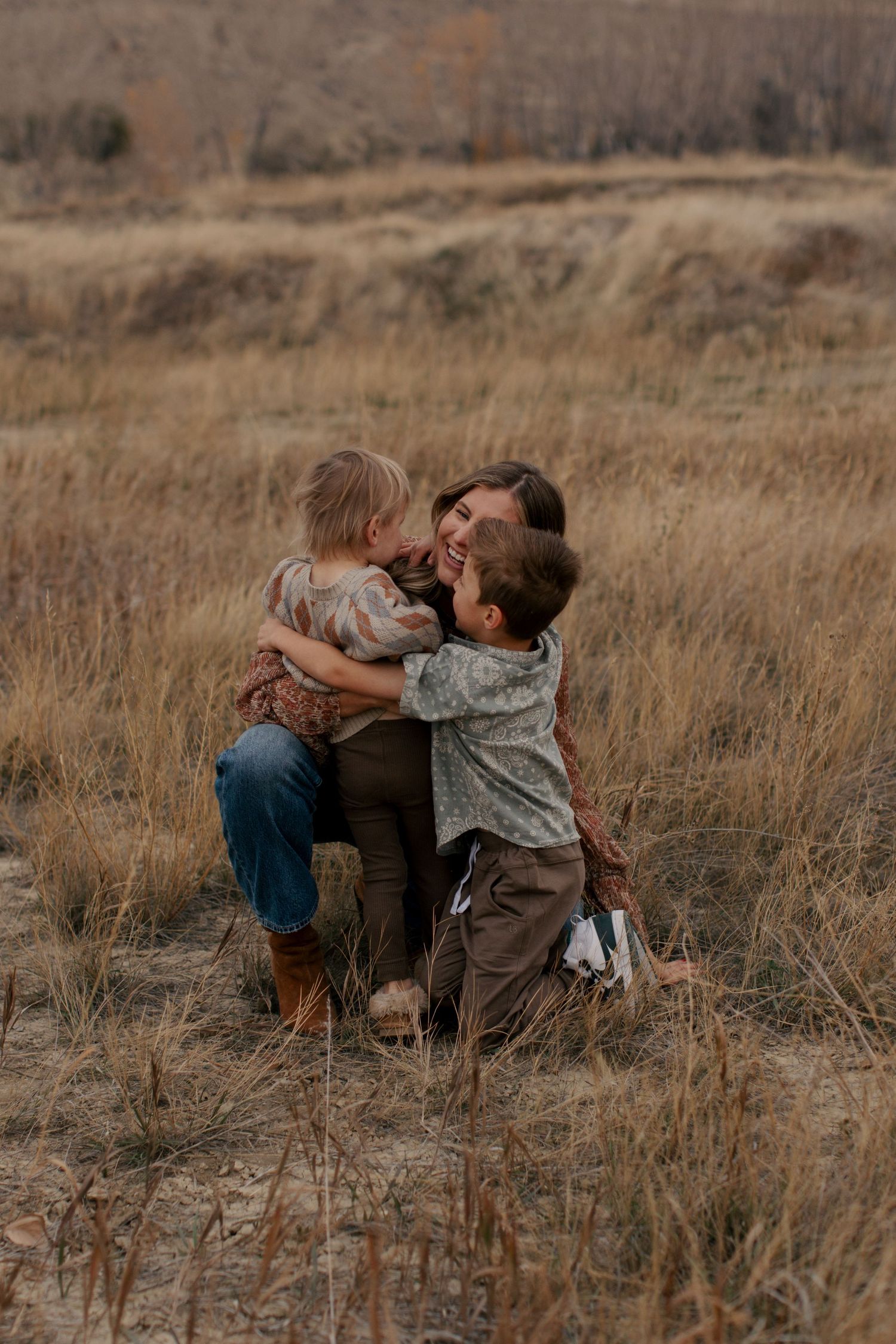 A sweet family moment captured in tall autumn grass during golden hour at sunset.