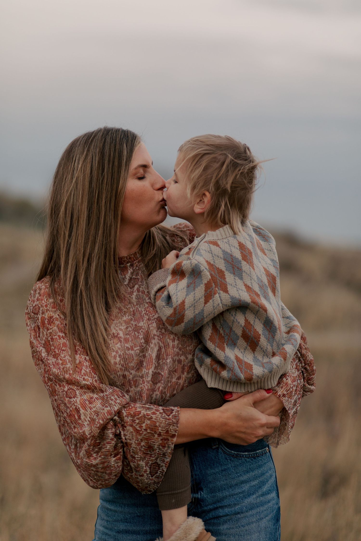 A tender moment shared between two people embracing in a wheat field at dusk wearing floral and plaid patterns.