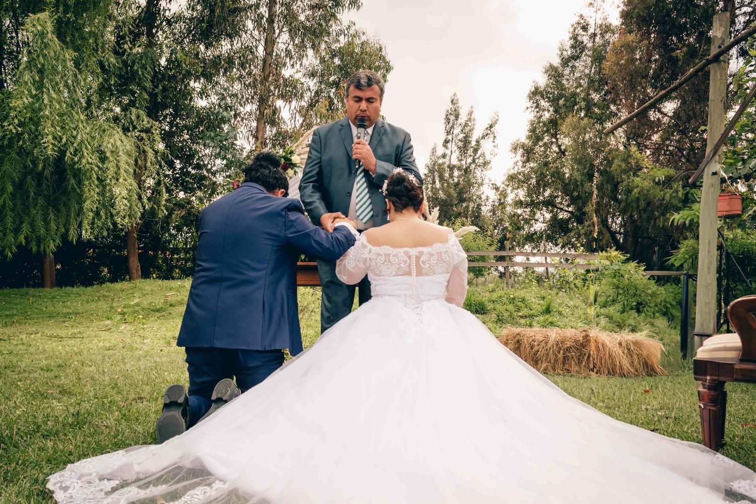 A bride and groom share a romantic dance moment outdoors under tall trees during their wedding celebration.