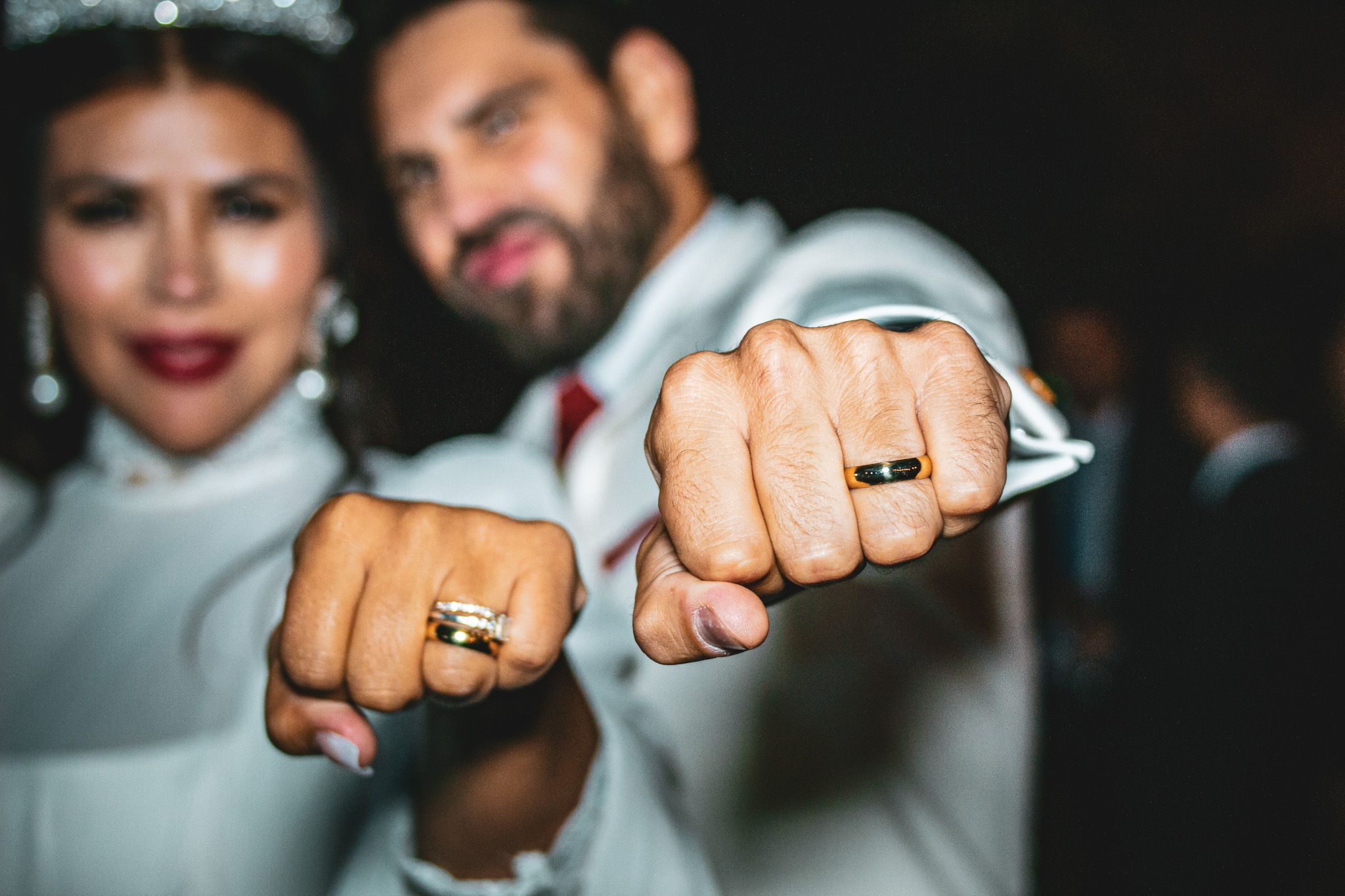 Primer plano de anillos de matrimonio mostrados sobre manos con fondo oscuro.