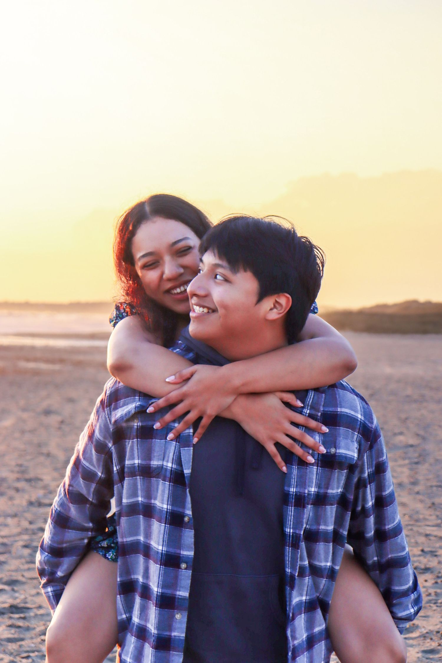 A couple shares a playful piggyback ride moment at sunset on the beach.