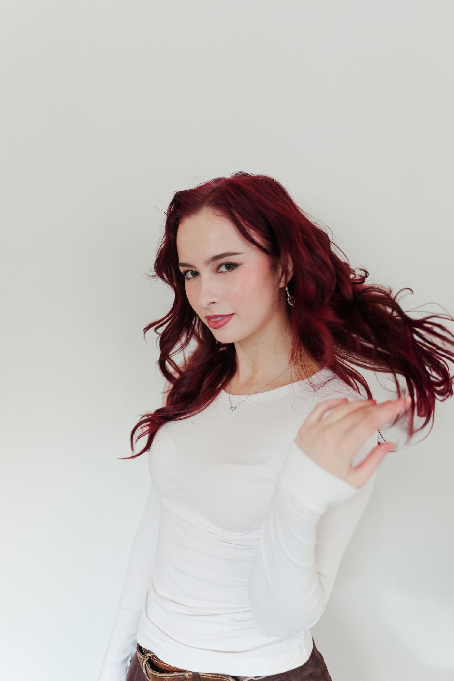 Portrait of woman with flowing red hair wearing white sweater against light background.
