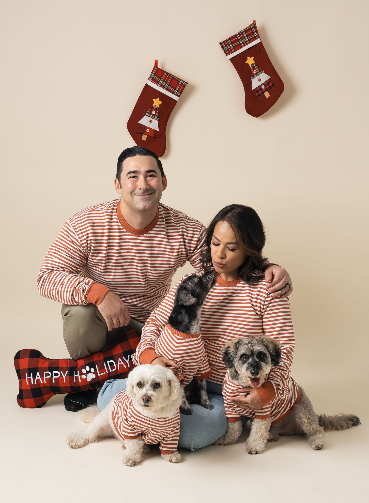 Family wearing matching striped outfits with their three pets and holiday decorations in a festive studio portrait.