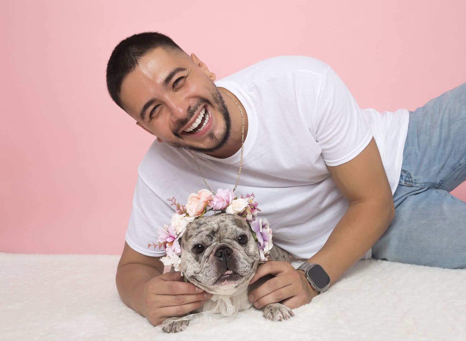 French bulldog lying on pink background while being pet on head showing companionship and affection.