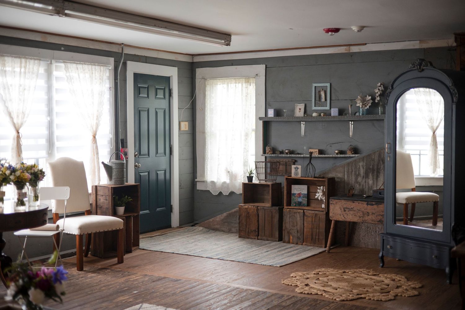 Rustic farmhouse living room interior with turquoise door, arched window, wooden furniture and floating shelves.