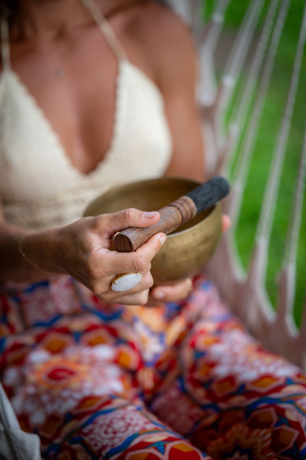 Person wearing flowy patterned clothing holds a wooden meditation bowl in a serene setting.