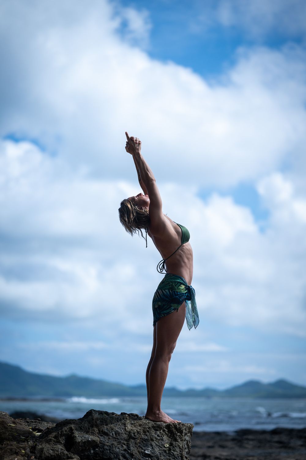 Yoga practitioner performs stretching poses against a scenic blue sky and rocky coastline backdrop.