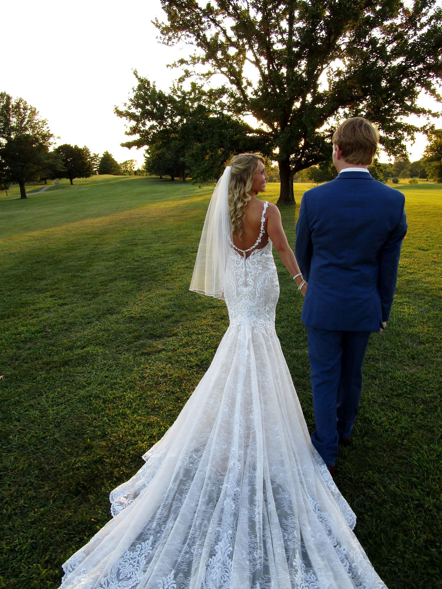 A bride and groom walk hand in hand toward the sunset