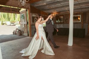 Dancing couple in formal attire twirling on rustic wooden floor with string lights overhead.