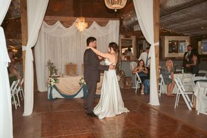 A couple shares their first dance in a decorated indoor reception venue with white draping and romantic lighting.