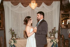 A couple shares their first dance at a wedding reception with twinkling lights and white drapes in the background.