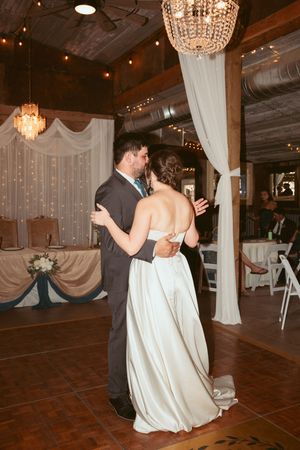 A couple shares their first dance under crystal chandeliers in an elegantly decorated rustic wedding reception venue.
